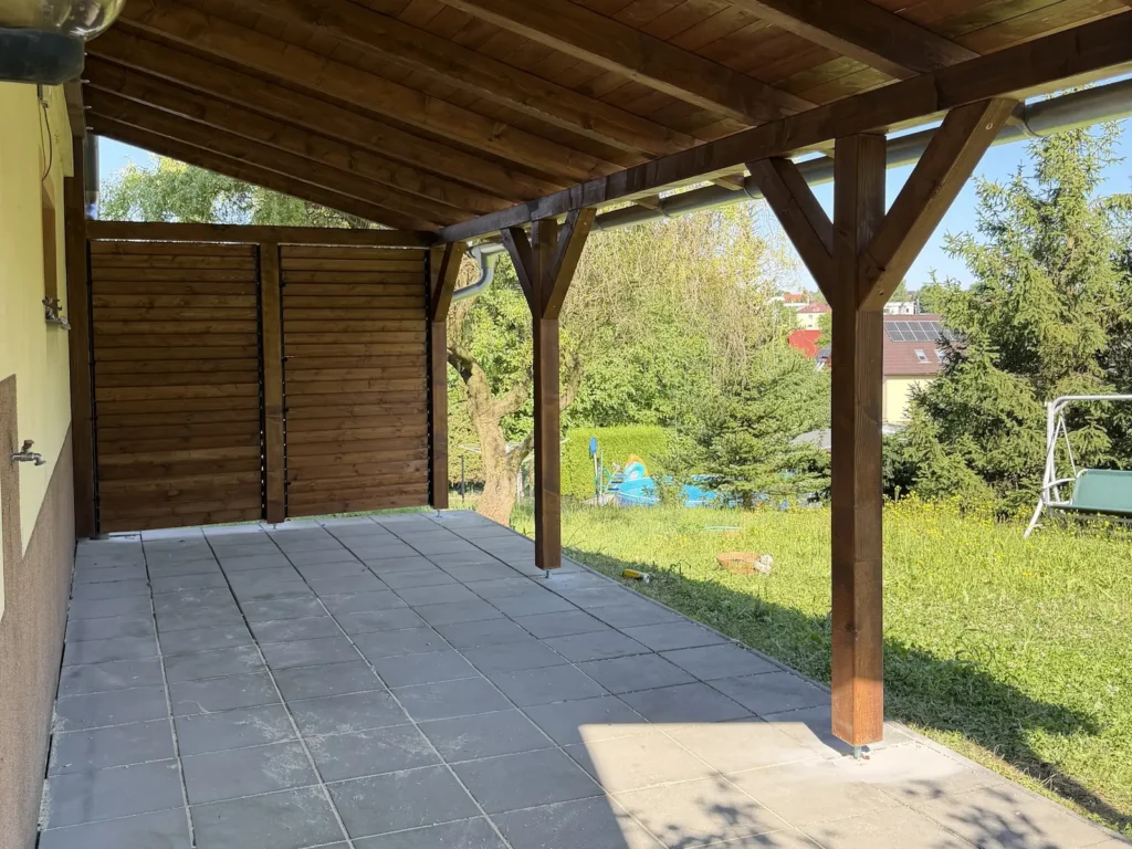 Kryté posezení pod pergolou s dřevěným podhledem a dvěma zavřenými poli otočných lamel